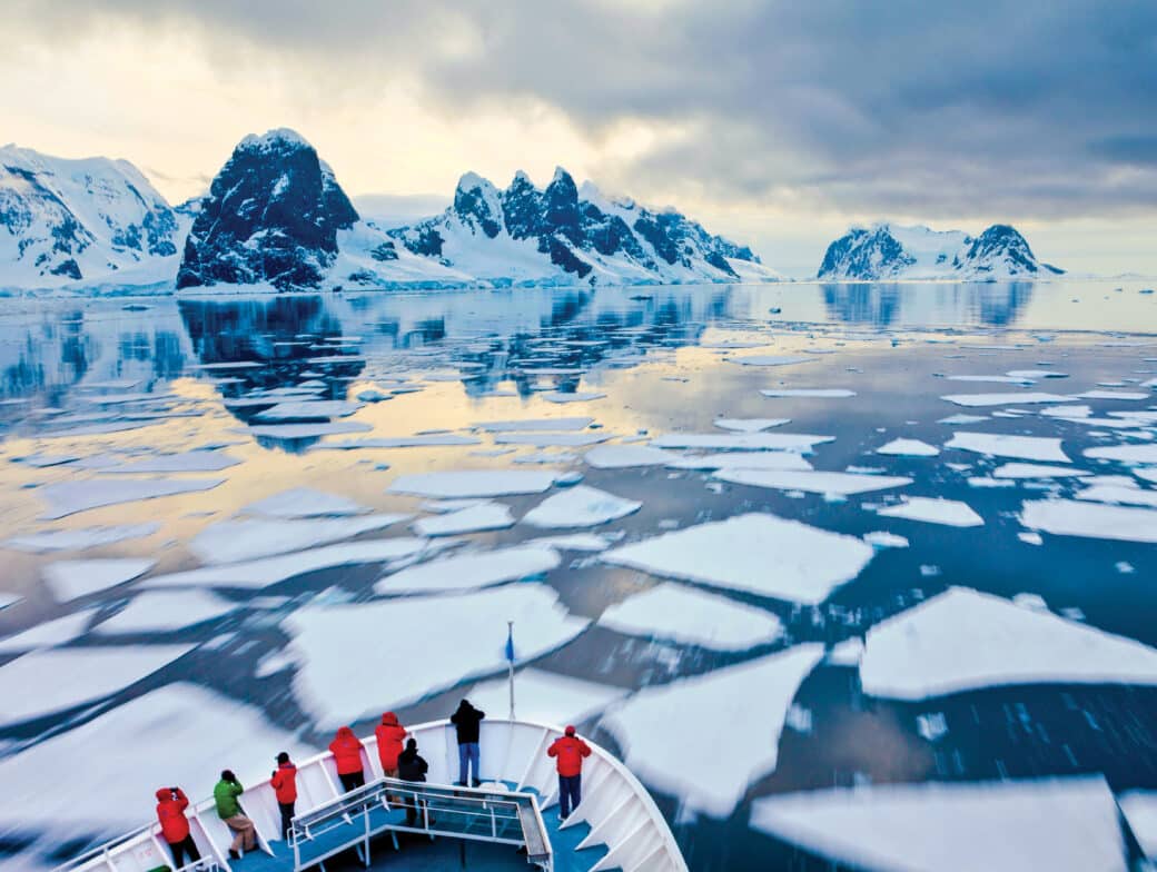 Passengers watch from the bow of a cruise ship as it goes through ice.