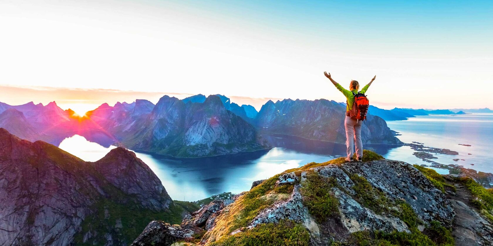 Happy woman hiker enjoying scenic view of midnight sun at the top of Reinebringen.